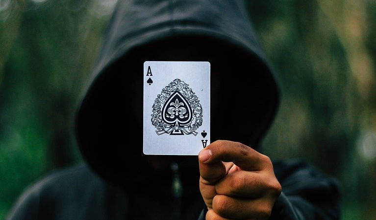 A hooded poker player holding an ace, likely demonstrating his ability to cheat.